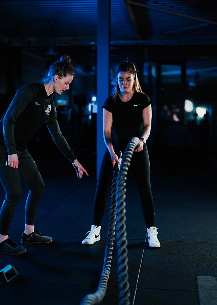 Coach moedigt een klant aan tijdens een training met battle ropes