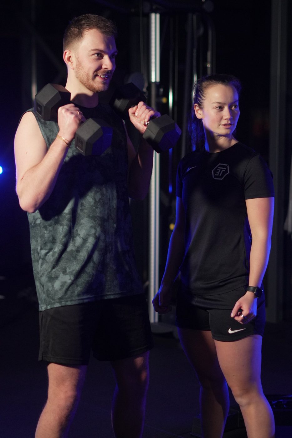 Coach kijkt mee terwijl een klant met dumbbells traint