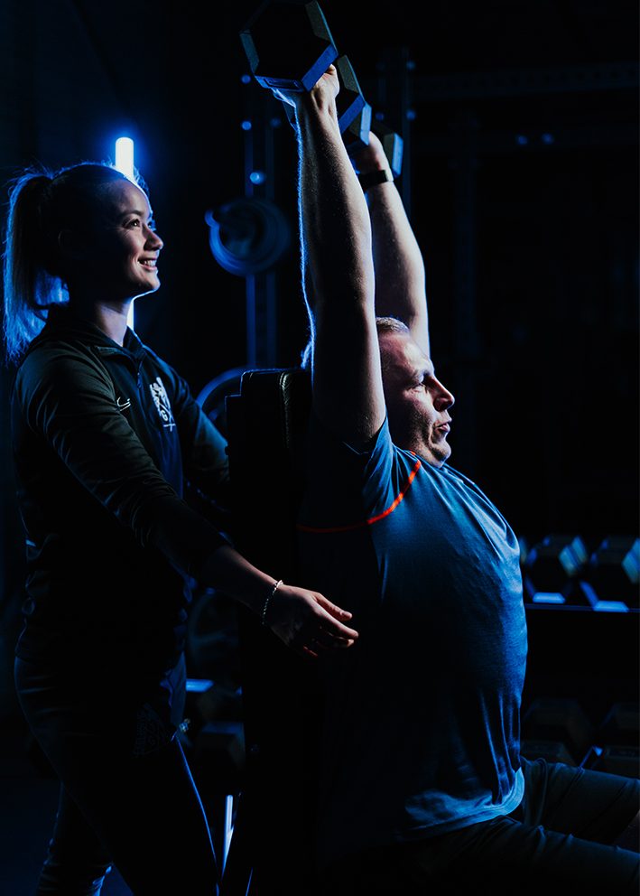 Lachende coach begeleidt een klant bij een overhead press