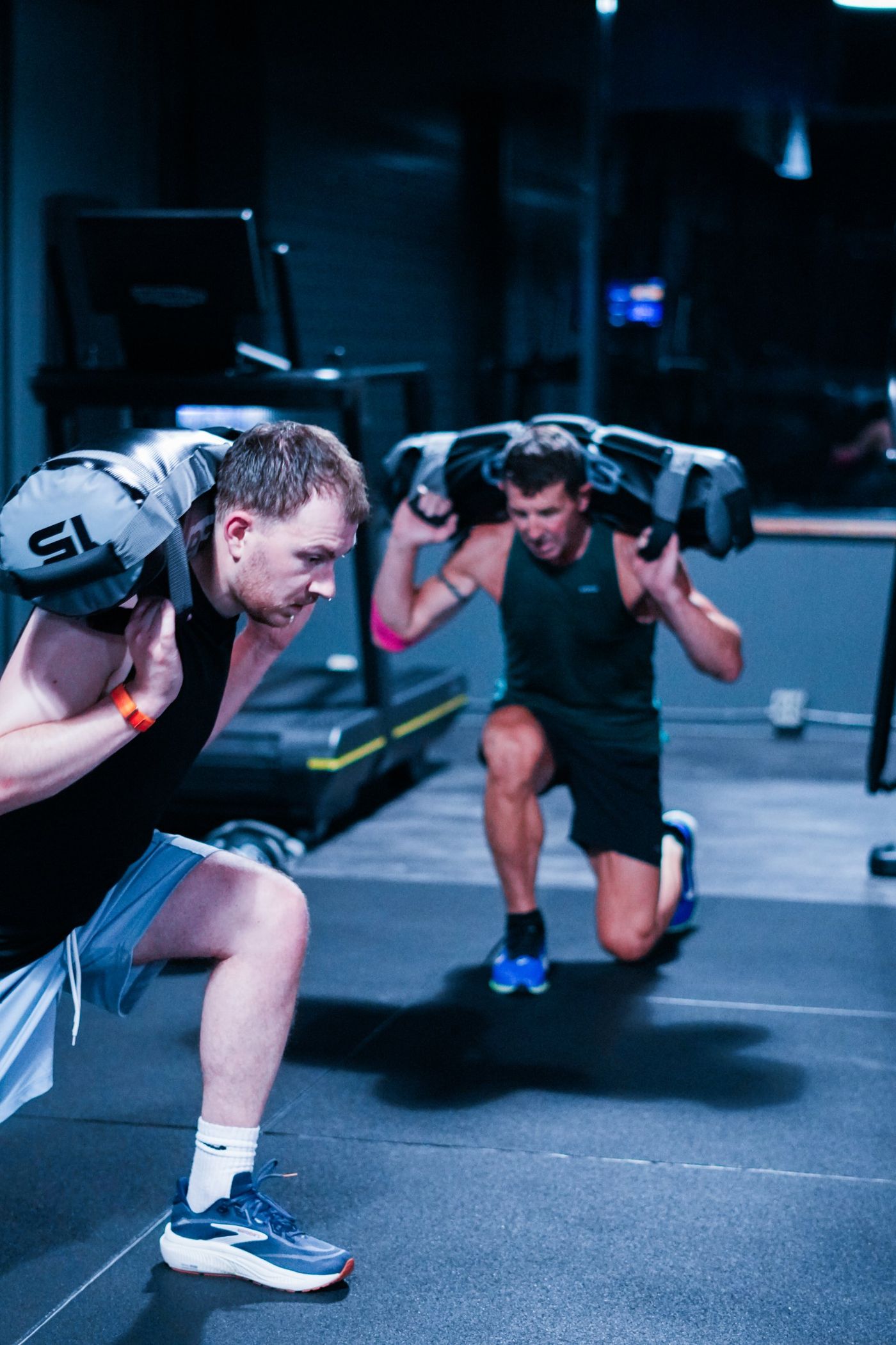 Twee mannen doen sandbag lunges tijdens een HYROX training