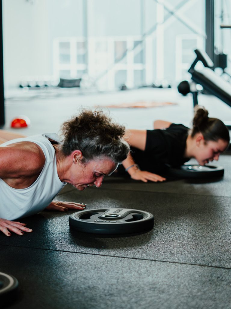 Twee vrouwen doen samen push-ups naast een halterschijf