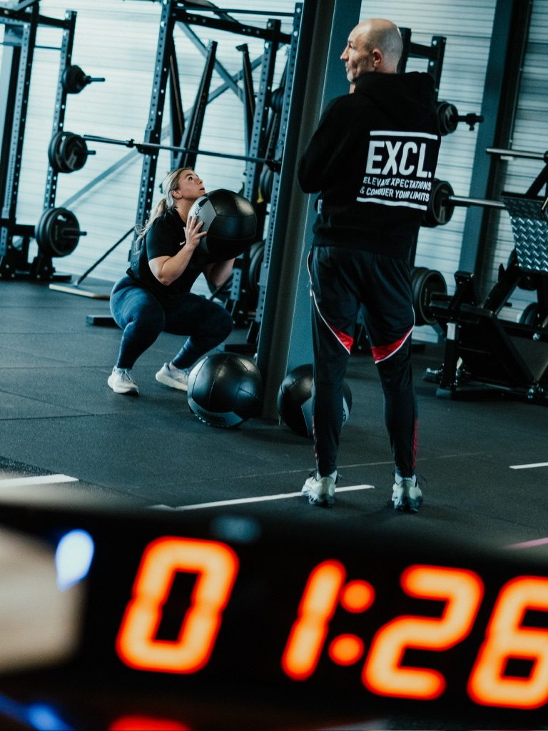 Coach kijkt mee terwijl een sporter een wall ball gooit
